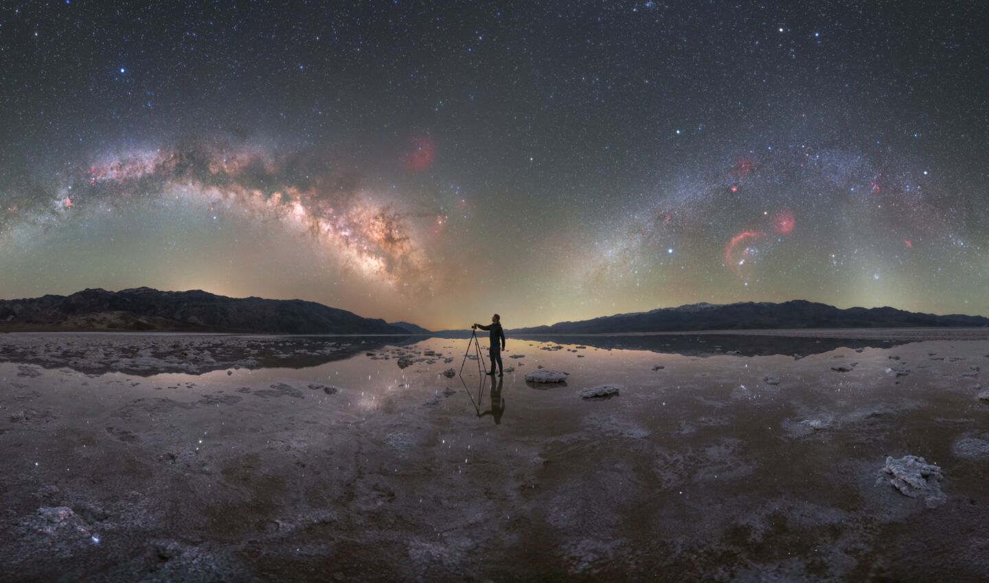 Photographer standing under Milky Way with sky reflected.